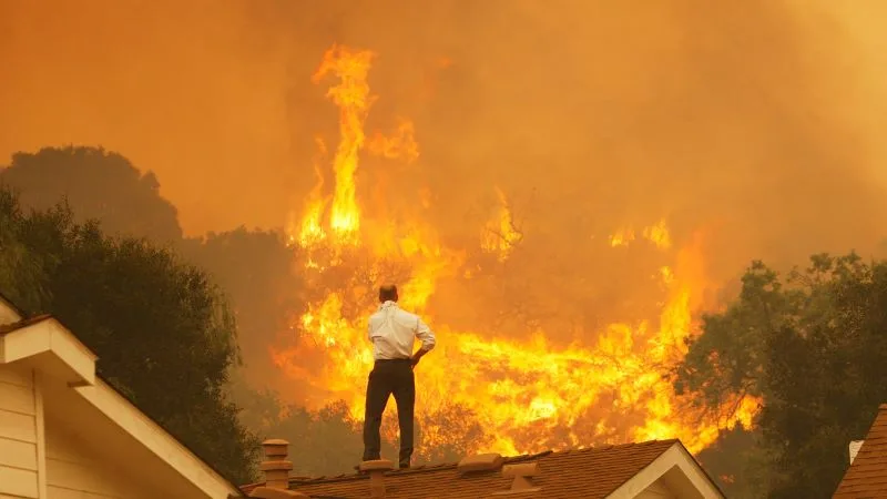 Man observing a devastating wildfire from his rooftop, a stark climate reality